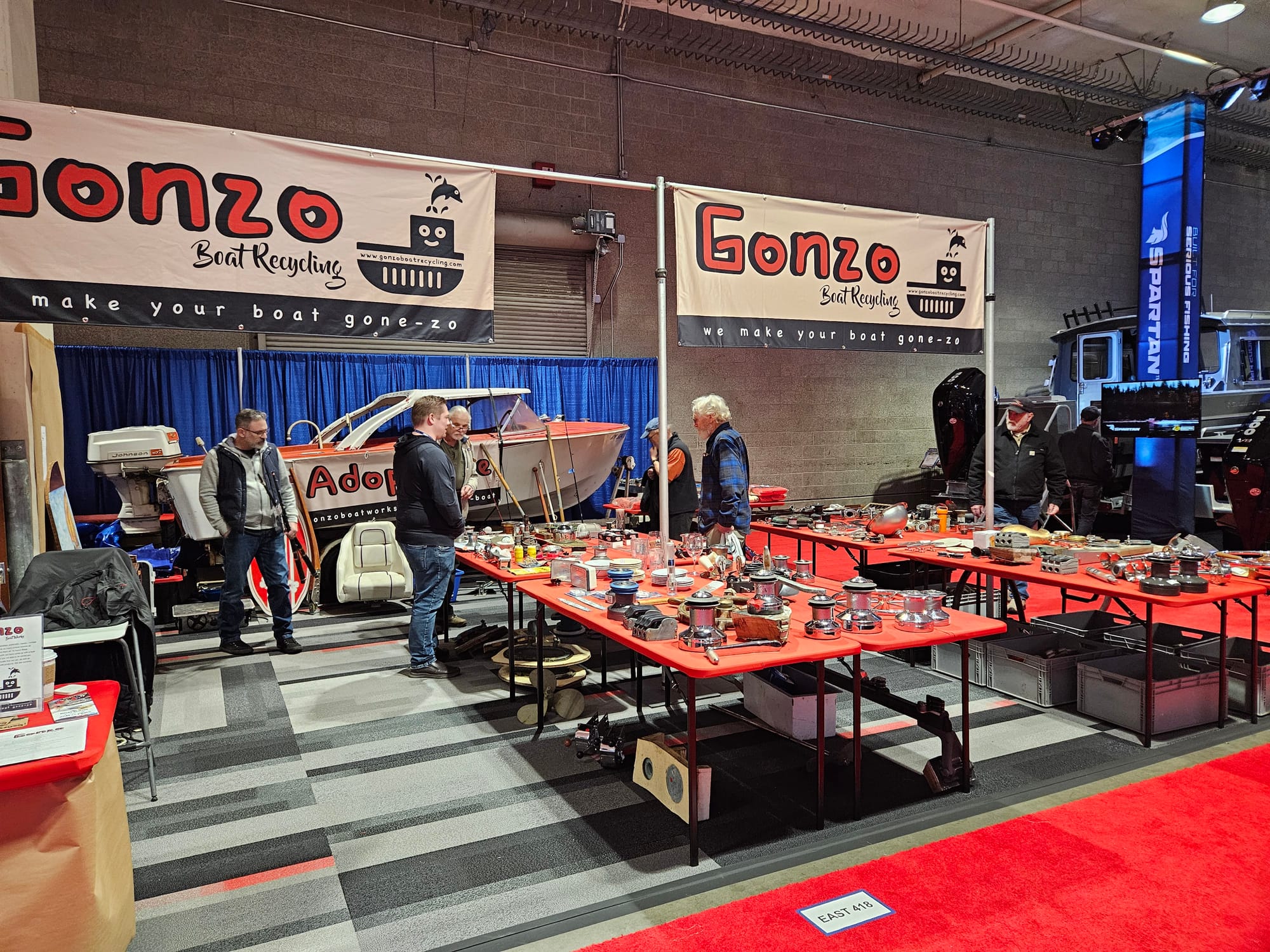 People browse tables covered in boat parts with signs that read "Gonzo Boat Recycling" above