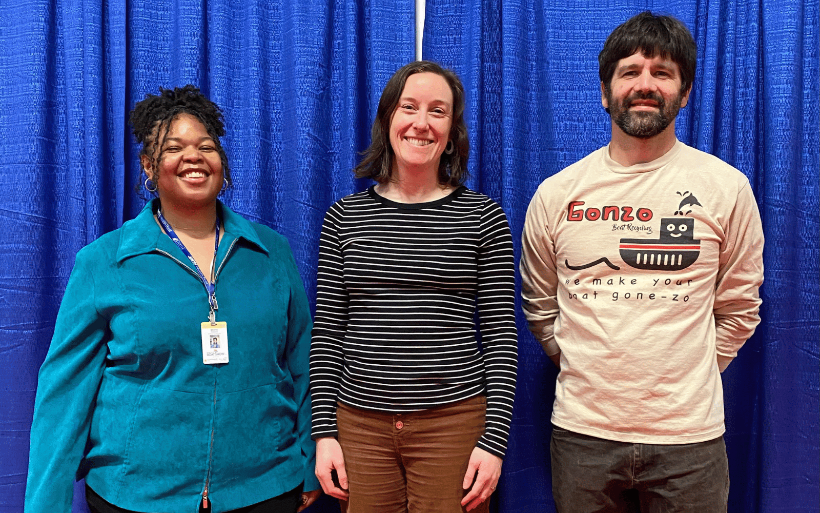 Three people stand side-by-side smiling in front of a blue curtain.