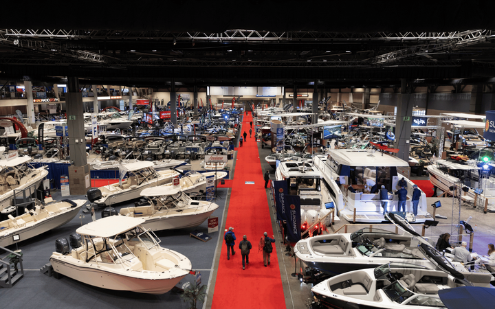 People walk down a red carpet in a large room filled with dozens of different boats.