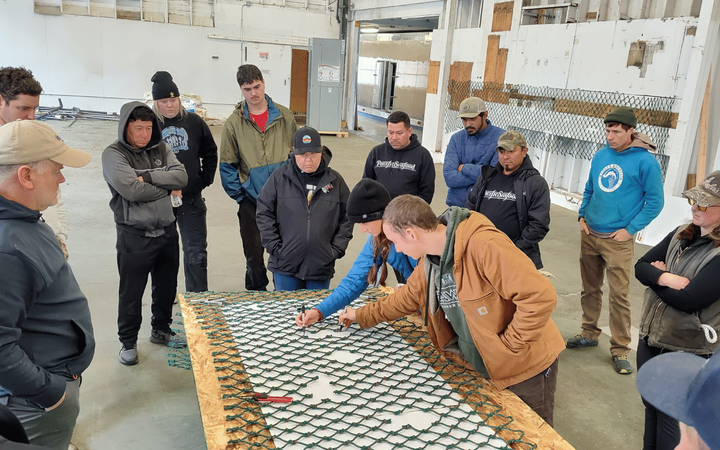 Two people lean over a net with holes while a dozen others look on.
